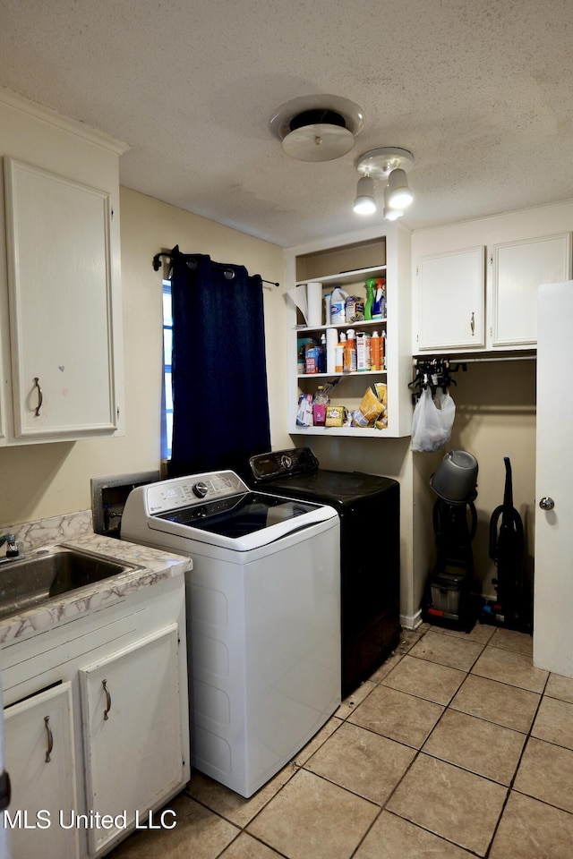 clothes washing area featuring washer and clothes dryer, a textured ceiling, a sink, cabinet space, and light tile patterned floors
