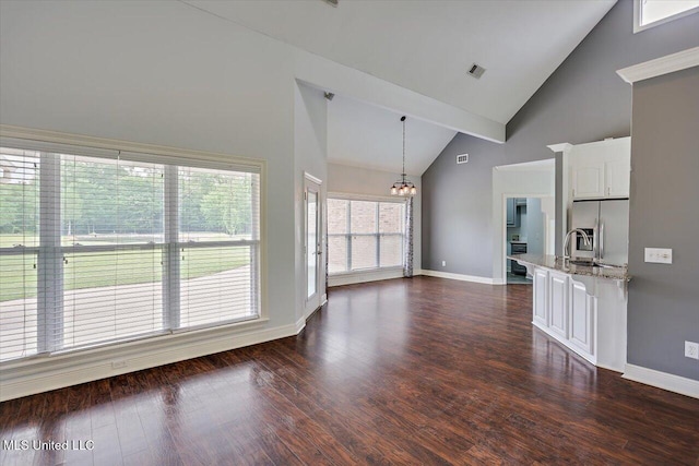 unfurnished living room featuring high vaulted ceiling, an inviting chandelier, dark wood-type flooring, and baseboards
