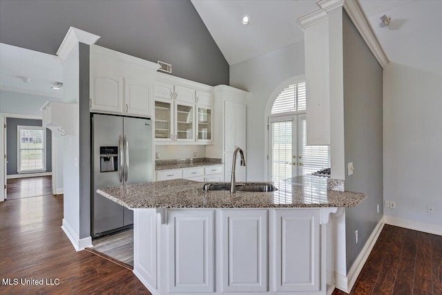 kitchen featuring light stone counters, stainless steel fridge, white cabinetry, and a sink