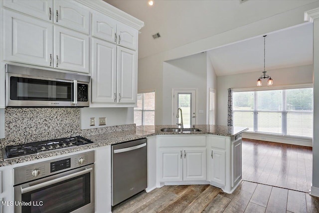 kitchen featuring stainless steel appliances, visible vents, a sink, light wood-type flooring, and a peninsula