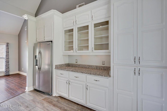 kitchen with white cabinets, lofted ceiling, glass insert cabinets, light stone counters, and stainless steel fridge with ice dispenser