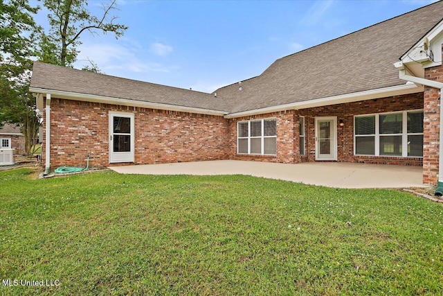 rear view of house featuring brick siding, a lawn, a shingled roof, and a patio
