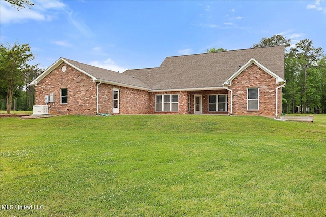rear view of house with roof with shingles, brick siding, and a yard