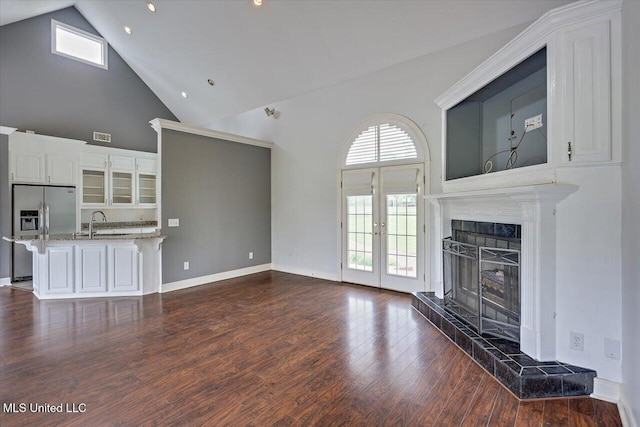 unfurnished living room with french doors, a sink, dark wood finished floors, a tiled fireplace, and high vaulted ceiling