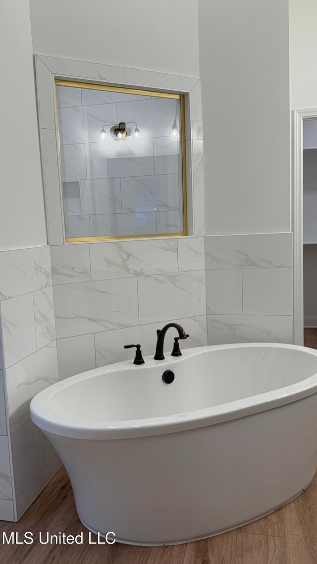 bathroom with wood-type flooring, a bath, and tile walls