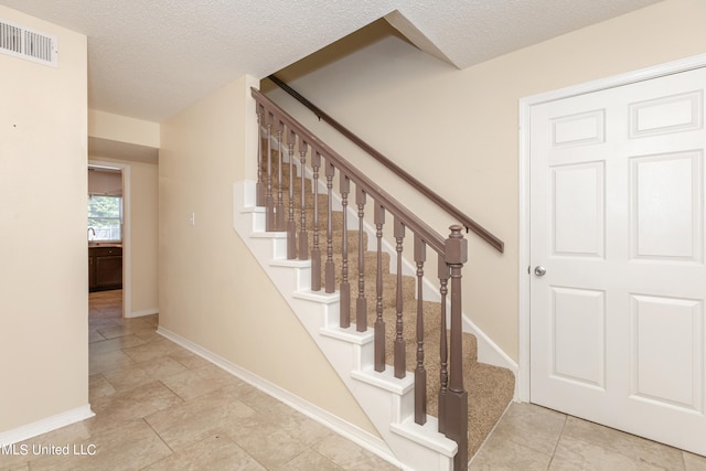 stairs with a textured ceiling and tile patterned flooring