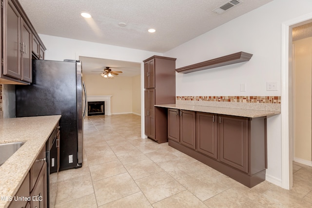 kitchen featuring light stone countertops, dark brown cabinetry, and ceiling fan