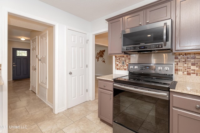 kitchen featuring light stone countertops, appliances with stainless steel finishes, backsplash, and light tile patterned floors