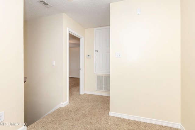 hall featuring a textured ceiling and light colored carpet