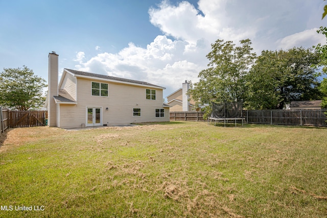 back of house with a trampoline and a lawn