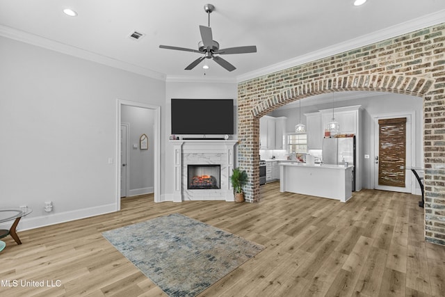 962 Glenwild Cir, Canton, MS 39046 - unfurnished living room with ceiling fan, light wood finished floors, a lit fireplace, arched walkways, and recessed lighting