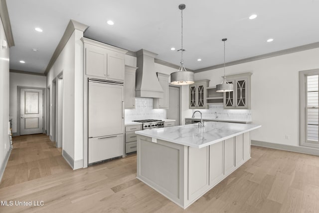 kitchen with paneled built in refrigerator, premium range hood, tasteful backsplash, a center island with sink, and recessed lighting