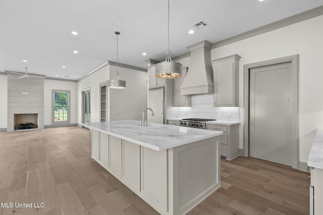 kitchen with custom exhaust hood, a fireplace, recessed lighting, light wood-style floors, and a center island with sink