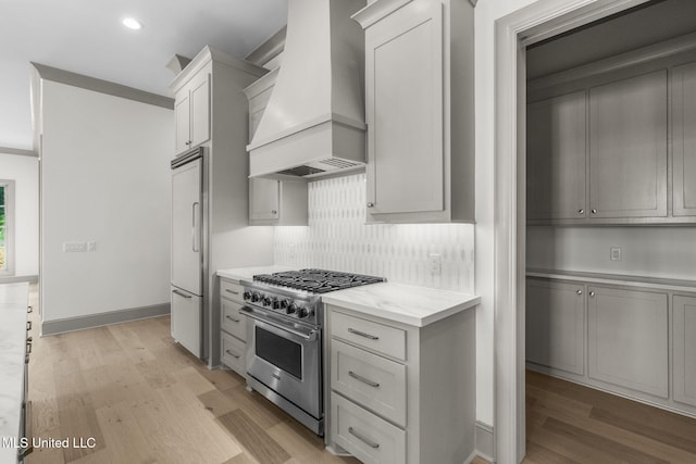 kitchen with premium appliances, custom exhaust hood, light wood-style floors, tasteful backsplash, and recessed lighting