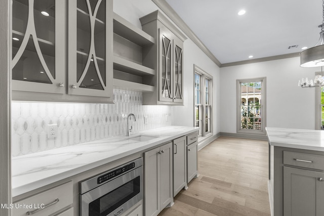 kitchen featuring gray cabinetry, stainless steel microwave, a sink, backsplash, and light stone counters