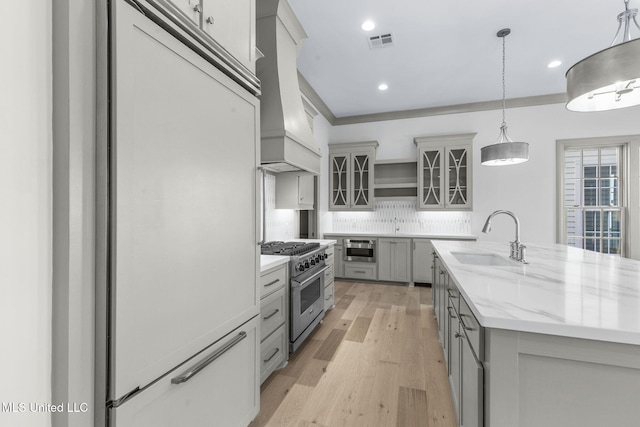 kitchen featuring premium appliances, a sink, gray cabinets, decorative backsplash, and light wood-style flooring