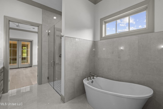 bathroom featuring tile walls, a stall shower, a soaking tub, and french doors
