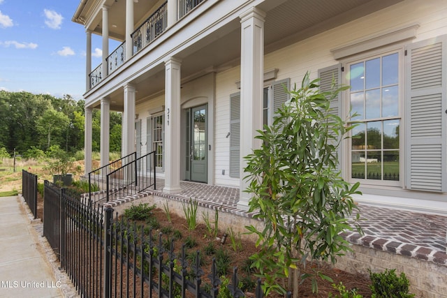 doorway to property featuring a porch, a balcony, and fence