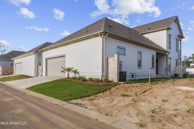 view of side of home with an attached garage, driveway, a lawn, and cooling unit