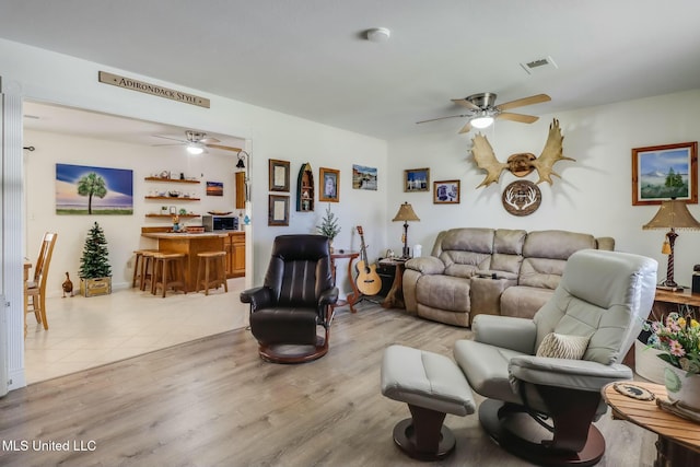 living room featuring a ceiling fan, visible vents, light wood-style flooring, and a bar