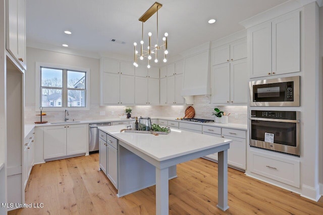 kitchen with sink, premium range hood, white cabinetry, pendant lighting, and stainless steel appliances