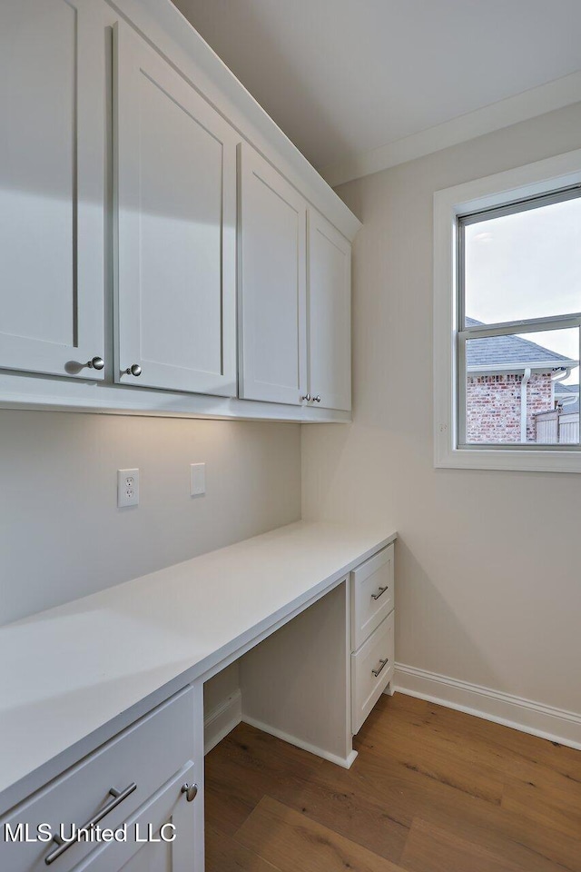 unfurnished office featuring crown molding, dark wood-type flooring, and built in desk