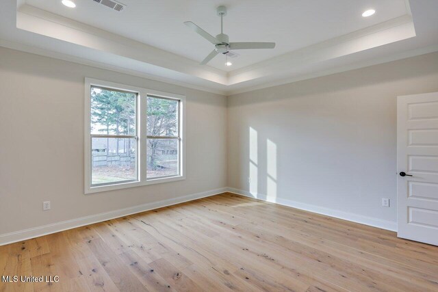 empty room with a tray ceiling, light hardwood / wood-style flooring, ornamental molding, and ceiling fan