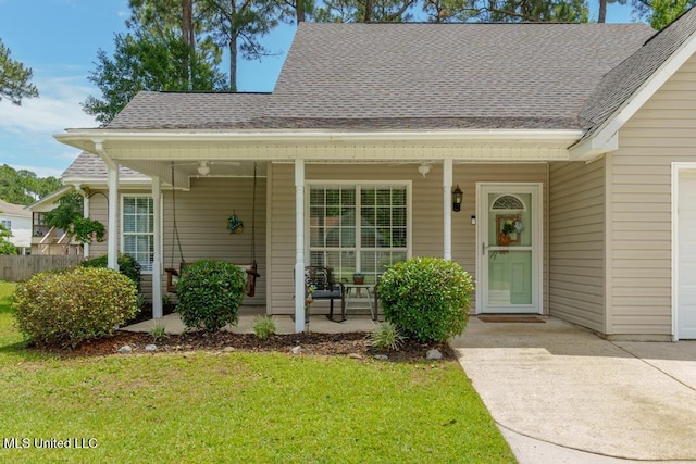 entrance to property featuring a porch, a lawn, a garage, and roof with shingles