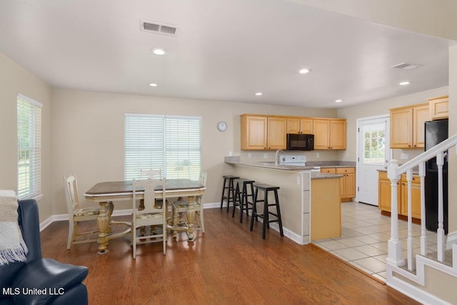 kitchen with black appliances, light brown cabinetry, a breakfast bar area, a peninsula, and recessed lighting