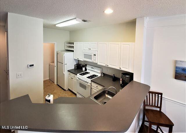 2252 Beach Dr Unit 1704, Gulfport, MS 39501 - kitchen with white appliances, a textured ceiling, dark countertops, washer and clothes dryer, and white cabinetry