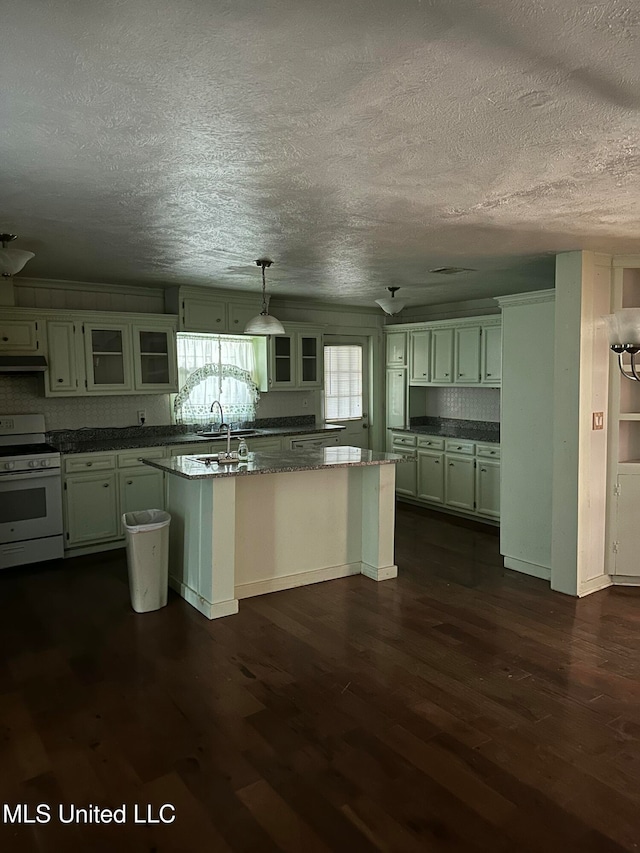 kitchen featuring dark hardwood / wood-style flooring, white gas stove, decorative light fixtures, and a center island with sink