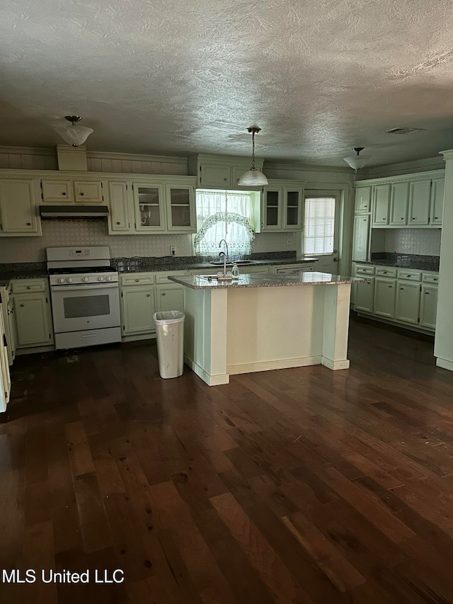 kitchen featuring pendant lighting, dark hardwood / wood-style flooring, white gas range, and an island with sink