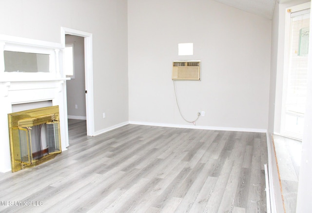 unfurnished living room featuring light wood-style floors, a wall mounted air conditioner, baseboards, and a glass covered fireplace