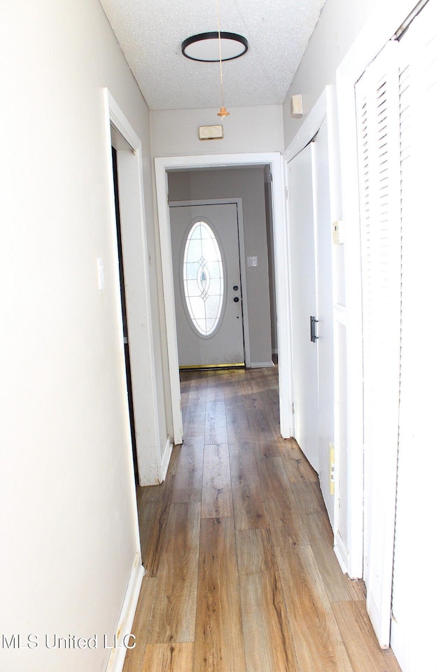 hall with light wood-style flooring, baseboards, and a textured ceiling