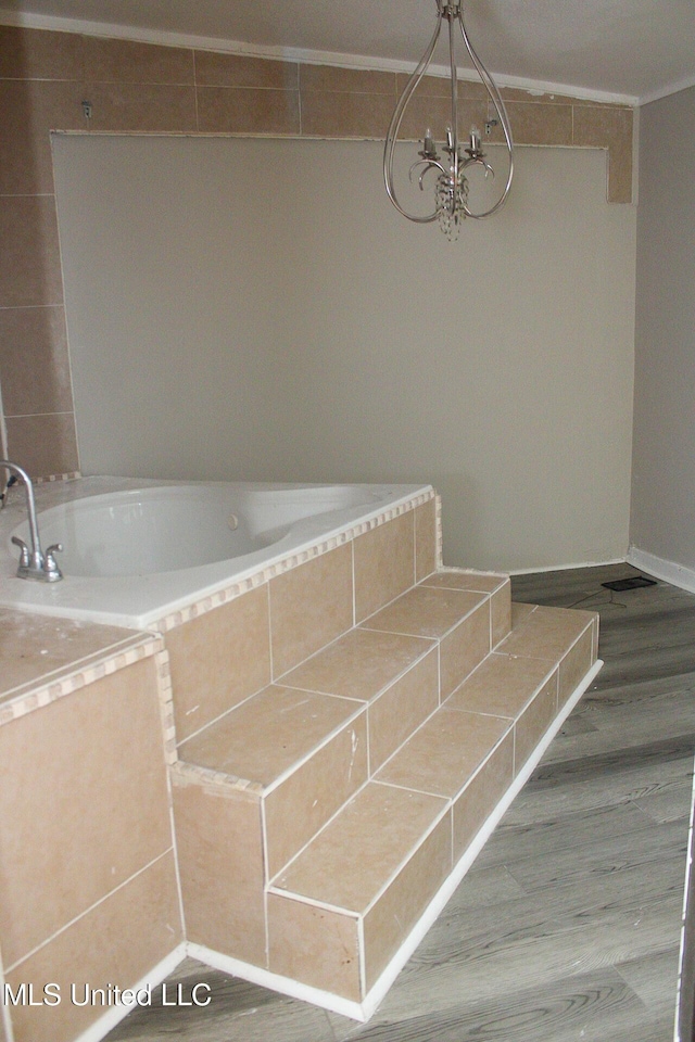 full bathroom with an inviting chandelier, tiled bath, baseboards, and wood finished floors