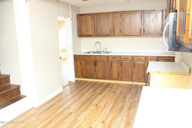 kitchen with brown cabinets, light wood-style flooring, light countertops, and a sink