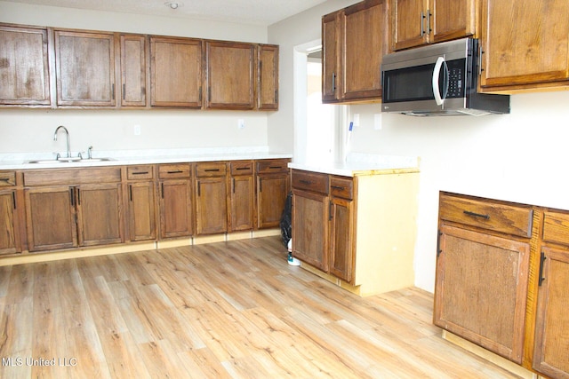 kitchen with brown cabinets, stainless steel microwave, light countertops, and a sink