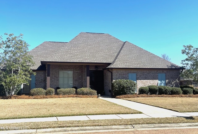 french country home with brick siding, a front lawn, and a shingled roof