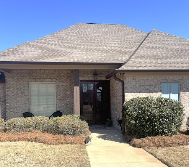 doorway to property featuring french doors, brick siding, and a shingled roof