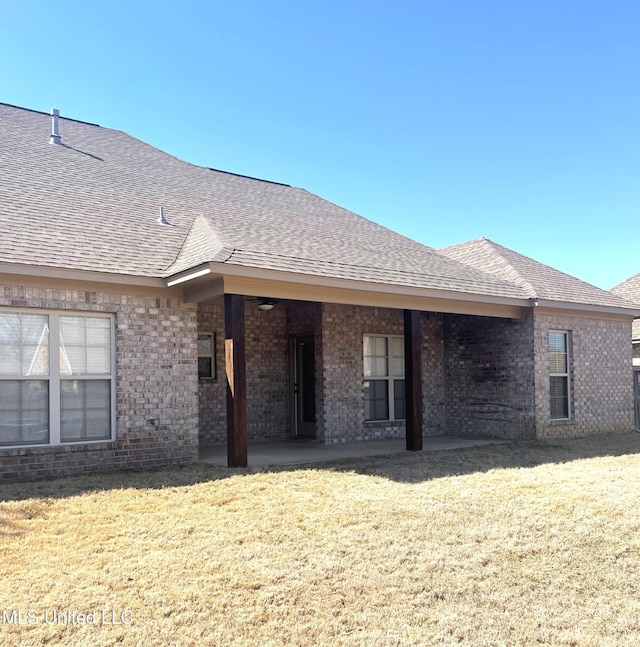 rear view of property with brick siding, a lawn, and a shingled roof