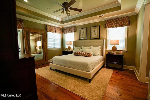 bedroom with a tray ceiling, visible vents, baseboards, and wood finished floors