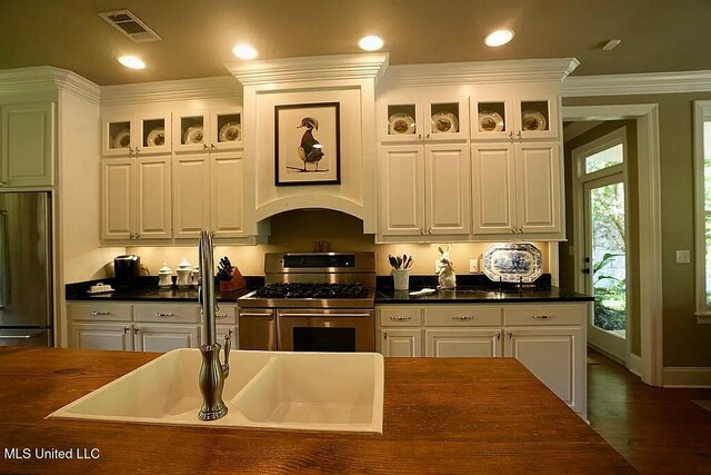 kitchen featuring visible vents, glass insert cabinets, appliances with stainless steel finishes, ornamental molding, and white cabinetry