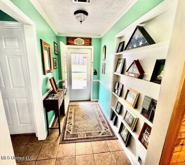 doorway with tile patterned flooring, built in features, a textured ceiling, and ornamental molding