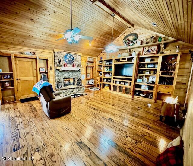 living room featuring wood ceiling, ceiling fan, wood finished floors, a stone fireplace, and wood walls