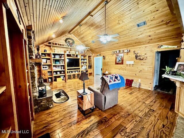 living room featuring lofted ceiling with beams, wooden ceiling, wood walls, wood finished floors, and a ceiling fan