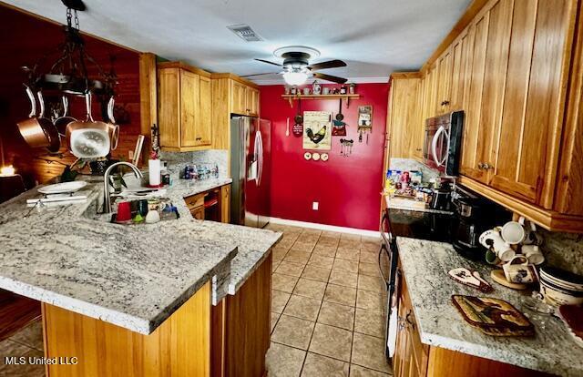 kitchen with light tile patterned floors, stainless steel appliances, a peninsula, a sink, and brown cabinets