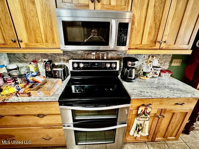 kitchen with appliances with stainless steel finishes, brown cabinetry, decorative backsplash, and light stone countertops