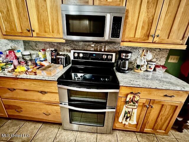 kitchen with appliances with stainless steel finishes, brown cabinetry, backsplash, and light stone counters