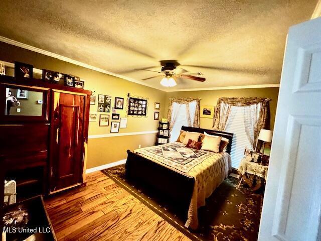 bedroom featuring crown molding, a textured ceiling, baseboards, and wood finished floors