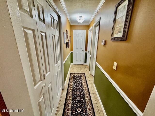 hall featuring light tile patterned floors, ornamental molding, a textured ceiling, and baseboards